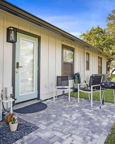 Modern single-story home exterior with patio, mint-green door, white desk setup, and tree-lined yard