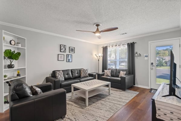 Bright living room with black leather sectional sofa, white coffee table, built-in shelving, and glass doors opening to backyard view